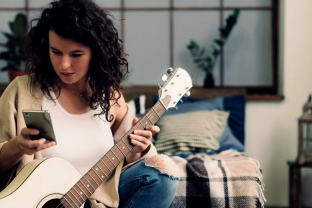 Moça sentada no sofá, pesquisando como aprender a tocar violão