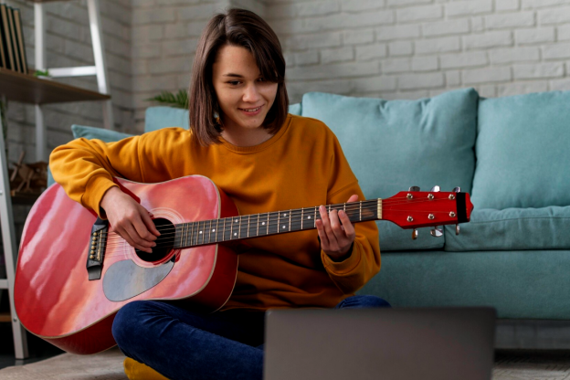 Moça diante do notebook, aprendendo com um professor de violão online
